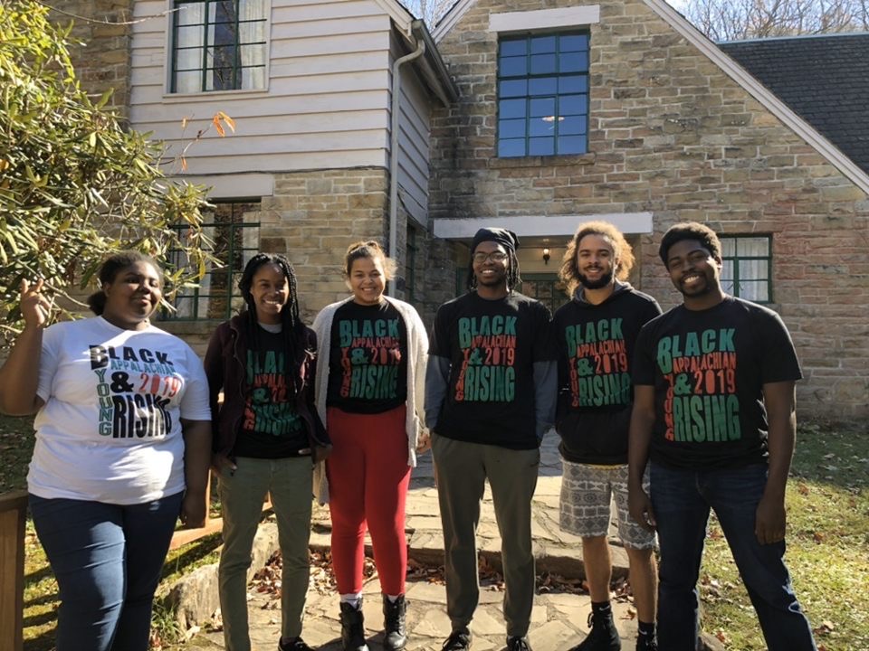 Six smiling Black young people stand in BAYR t-shirts outside in the sun